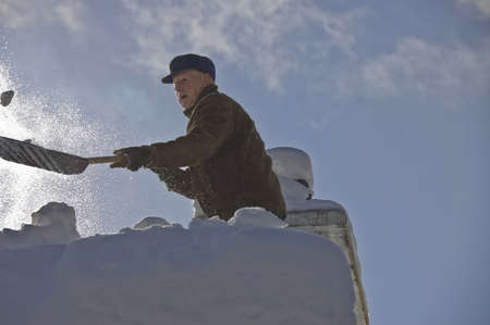 Senior shovelling his roof after a snow storm の写真素材