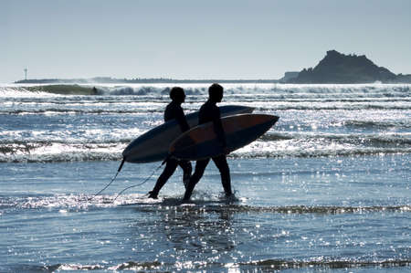 Silhouettes surfers at sunset on California beach going back home