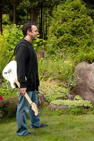 mature sexy man standing in the garden with a guitar on his shoulderの写真素材