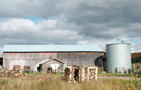 old rustic barn with silo and woods pile in Quebec Country  in autumn, Canadaの写真素材