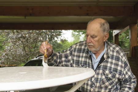 aged senior man with expressive face painting carefully  a garden  tableの写真素材