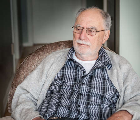 portrait of a grandfather wearing a gray sweater sit on an armchair at home