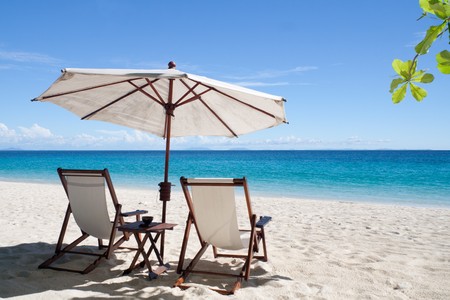 Deckchairs and parasol on the white sand beach facing the lagoonの写真素材