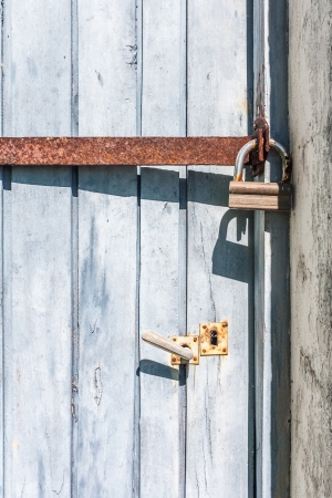 Old wooden door closed with an iron bar and a padlockの写真素材