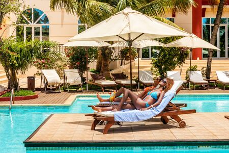 Two women sunbathing on sunbeds by the poolの写真素材