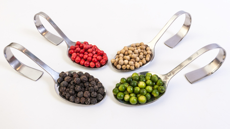 Four kinds of peppercorns in metallic spoons isolated on white backgroundの写真素材