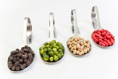 Four kinds of peppercorns in metallic spoons isolated on white backgroundの写真素材