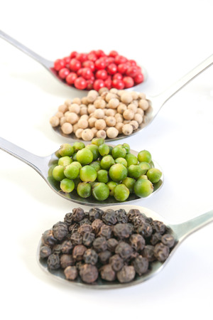 Four kinds of peppercorns in metallic spoons isolated on white backgroundの写真素材