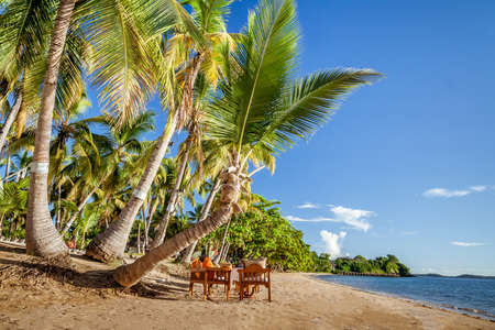 Wooden tables with armchairs and benches at a luxury resort close to a tropical beachの写真素材