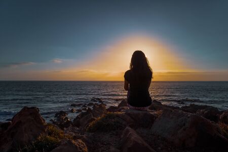 A woman praticing the lotus posture of Hatha yoga at sunset in front of the beachの写真素材