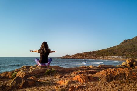A woman praticing the lotus posture of Hatha yoga in front of the beachの写真素材