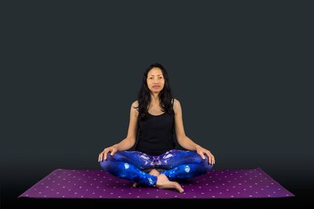 A woman yoga teacher in sukhasana posture isolated on black backgroundの写真素材