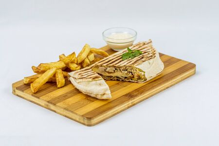 Shawarma sandwich, fresh roll in lavash with French fries. Kebab served on wooden board.の写真素材