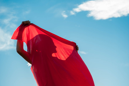 woman wrapped in a red scarf in the windの写真素材