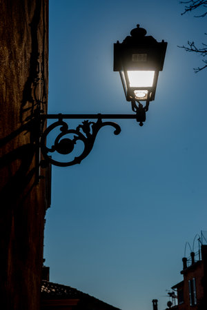 Old wrought iron lamppost lit with the cathedral of Brescia in the backgroundの写真素材