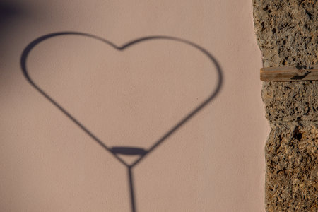 Metal heart reflecting the shadow against the wallの写真素材