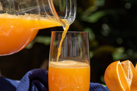 Orange juice pouring into a glass with fresh fruits in the background.の写真素材
