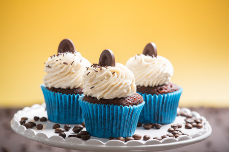 three cupcakes with chocolate and cream with coffee beans on the yellow backgroundの写真素材