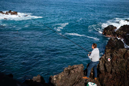 Tenerife, Spain - December 15, 2019: A fisherman at the coast of Puerto de la Cruz.