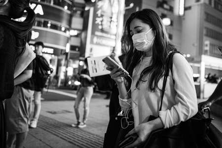 Tokyo, Japan - September 17, 2019: A Japanese girl with a face mask looking at her mobile phone on the street.のeditorial素材