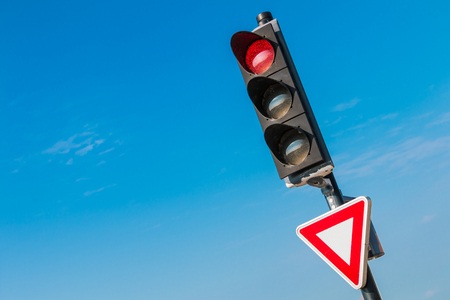 red traffic light with yield sign on blue skyの写真素材