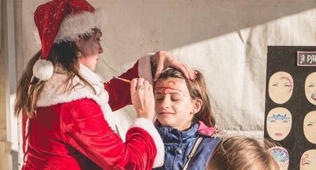 Bretignolles sur Mer, France - December 18, 2016 : During the Christmas period, a little girl is applying makeup in a stand on a Christmas marketのeditorial素材