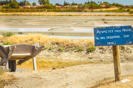 wooden wheelbarrow in front of salt marshes and a wooden panels is written in French "Respect my Marsh - Do not get down please -  Thank you"のeditorial素材