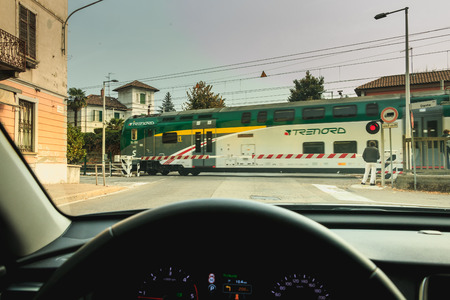 Fino Mornasco, Italy - November 04, 2017 : driver watches the passage of a train behind the gates of a railroad crossing on a fall dayのeditorial素材