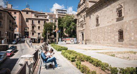 Toledo, Spain - April 28, 2018: tourists sitting on a bench in front of Santa Cruz de Toledo on a...