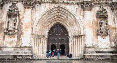 Alcobaca, Portugal - April 13, 2019: People walk in the rain in front of Alcobaca Monastery,...