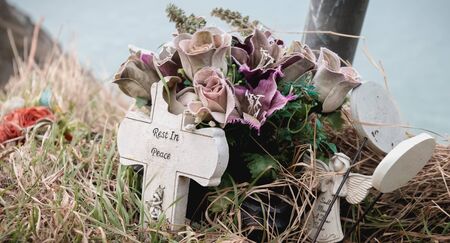 rest in peace written in English on a cross at the edge of a cliff