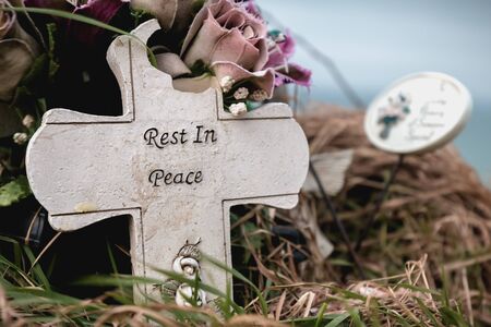 rest in peace written in English on a cross at the edge of a cliffの写真素材