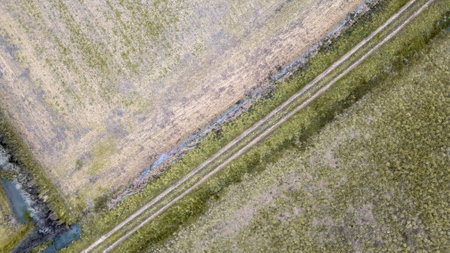 Dirt road in the countryside surrounded by wintering fields in France seen by droneの写真素材