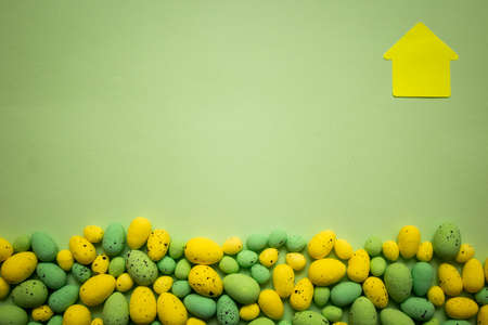 Yellow and green Easter eggs on green background with yellow house of paper. Spring holidays conceptの写真素材