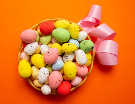 Colorful Easter eggs in the basket with pink ribbon on orange background. Spring holidays concept