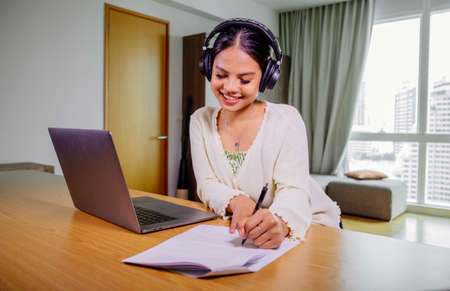 Beautiful young smiling asian woman working on laptop in living room at home. Asia business woman...