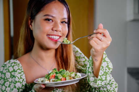 beautiful young asian woman eating healthy mediterranean food. smiling happy girl eating greek saladの写真素材