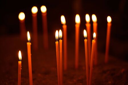 long lighted candles group on dark background.