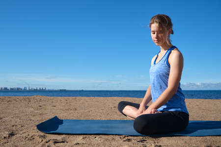 Young slim girl doing yoga on the beach on a sunny morning, positive attitude, healthy lifestyle