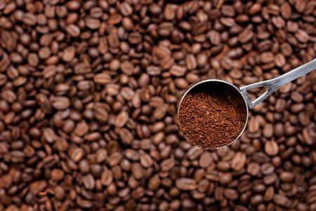 Scoop with ground coffee (focus on it) over coffee beans.の写真素材