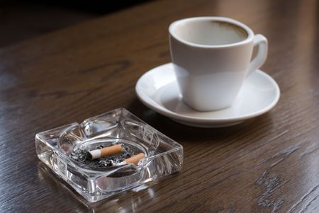 Ashtray and empty coffe cup on the cafe table. Shallow depth of field (focus on the cigarette butt).の写真素材