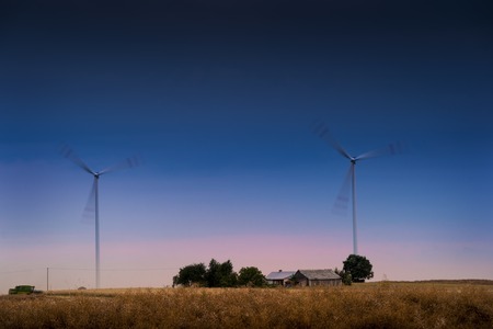 Windfarm adn house - wind turbines spinning on the field at dusk.の写真素材