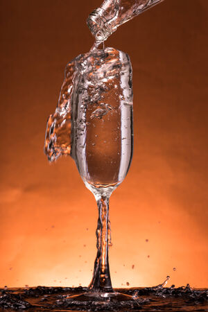 Water is poured into the  glass on orange backgroundの写真素材