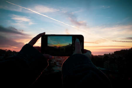 hands taking picture at sunset with phoneの写真素材