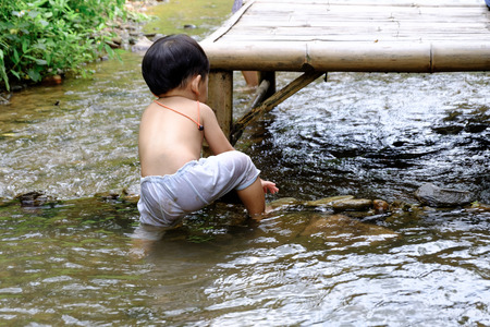 The boy playing in the river trying to climb up from river with his  little stone damのeditorial素材