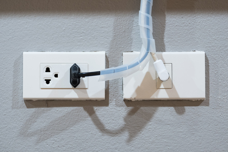 Electrical plug (left) and TV signal plug (right) on grey cement background