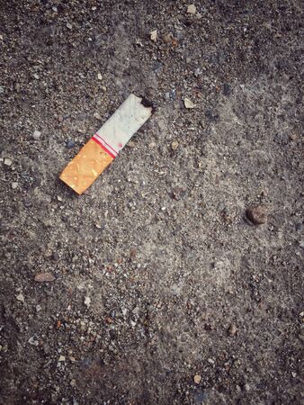 Burnt cigarette stub butt on dirty sand ground floor, vintage effect