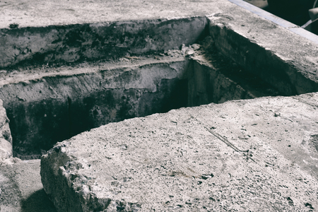 Opened old and dirty concrete manhole cover on pavement, vintage effectの写真素材