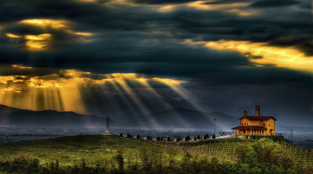 Spectacular blades of light filter through the dramatic clouds that dominate the Partisan Shrine of Bastia Mondovi ', in the Langhe, Piedmont, Italy.の写真素材