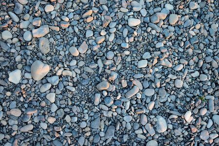 A closeup of a pile of loose rounded gray stones lying on a riverbank. The pebbles are used as a construction aggregate for pouring a concrete foundation. The rocks are cobblestones of various sizes, which are mostly gray with a slight blue or yellow color tone. The rounded stones and the uneven surface create an abstract pattern which is well usable for backgrounds and textures, resembling solid even being loose.の写真素材